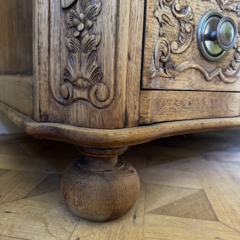 Close-up of a wooden cabinet with intricate carvings and a knob on a wooden floor.